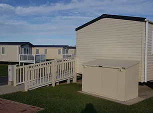 A rear view of a trailer park cabin with a ramp and external storage cabinet.