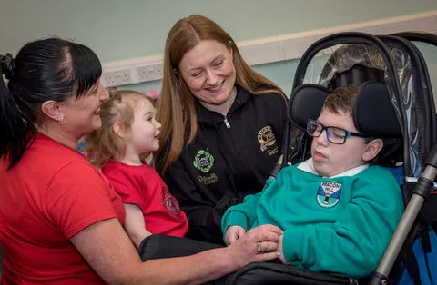 Two women and a young girl are smiling and looking at a young boy in a push chair.